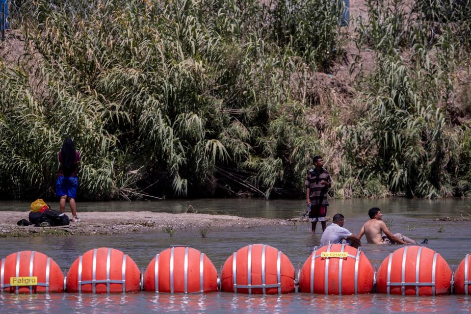 Migrants rest near Buoys on the U.S. side of the Rio Grande in Eagle Pass, Texas on July 20, 2023. The buoys were installed on orders by Texas Governor Greg Abbott to prevent migrants from reaching the north embankment of the Rio Grande on the international boundary between Mexico and the U.S.
